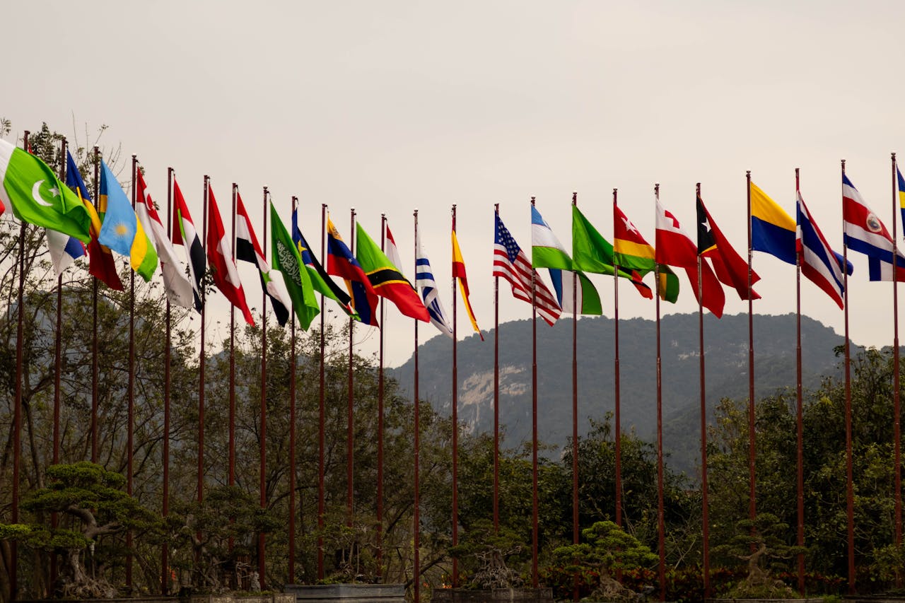 about-01 A display of various national flags on flagpoles set against a mountain backdrop, symbolizing global unity.