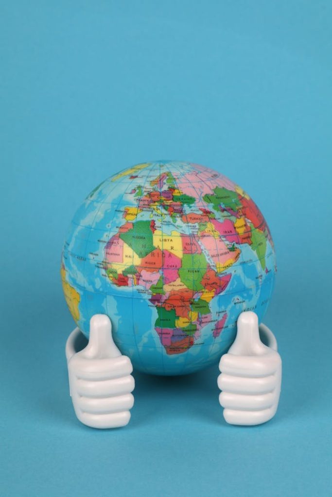 globe-and-hands-with-thumbs-up-22669710 A colorful globe held by two thumbs up hands against a vibrant blue background.