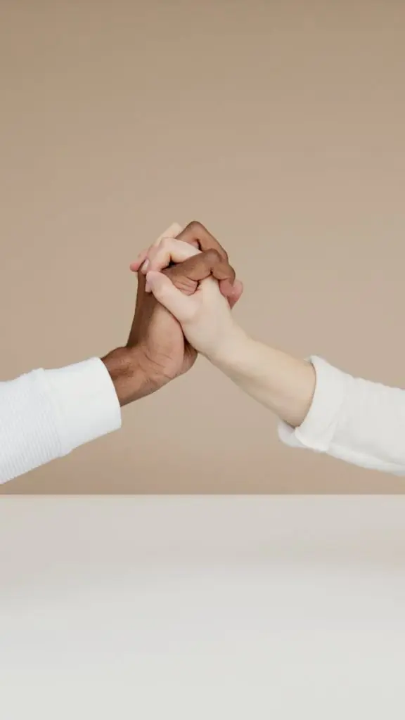 Close-up of two diverse hands gripping in a gesture of unity on a neutral background.